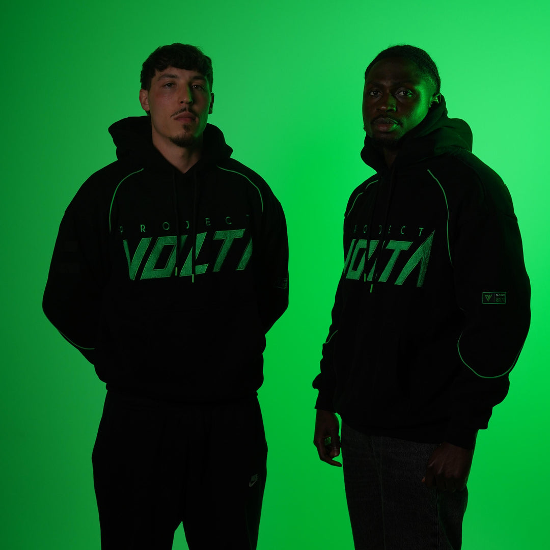Two people wearing black hoodies with 'Project Volta' logo against a green background