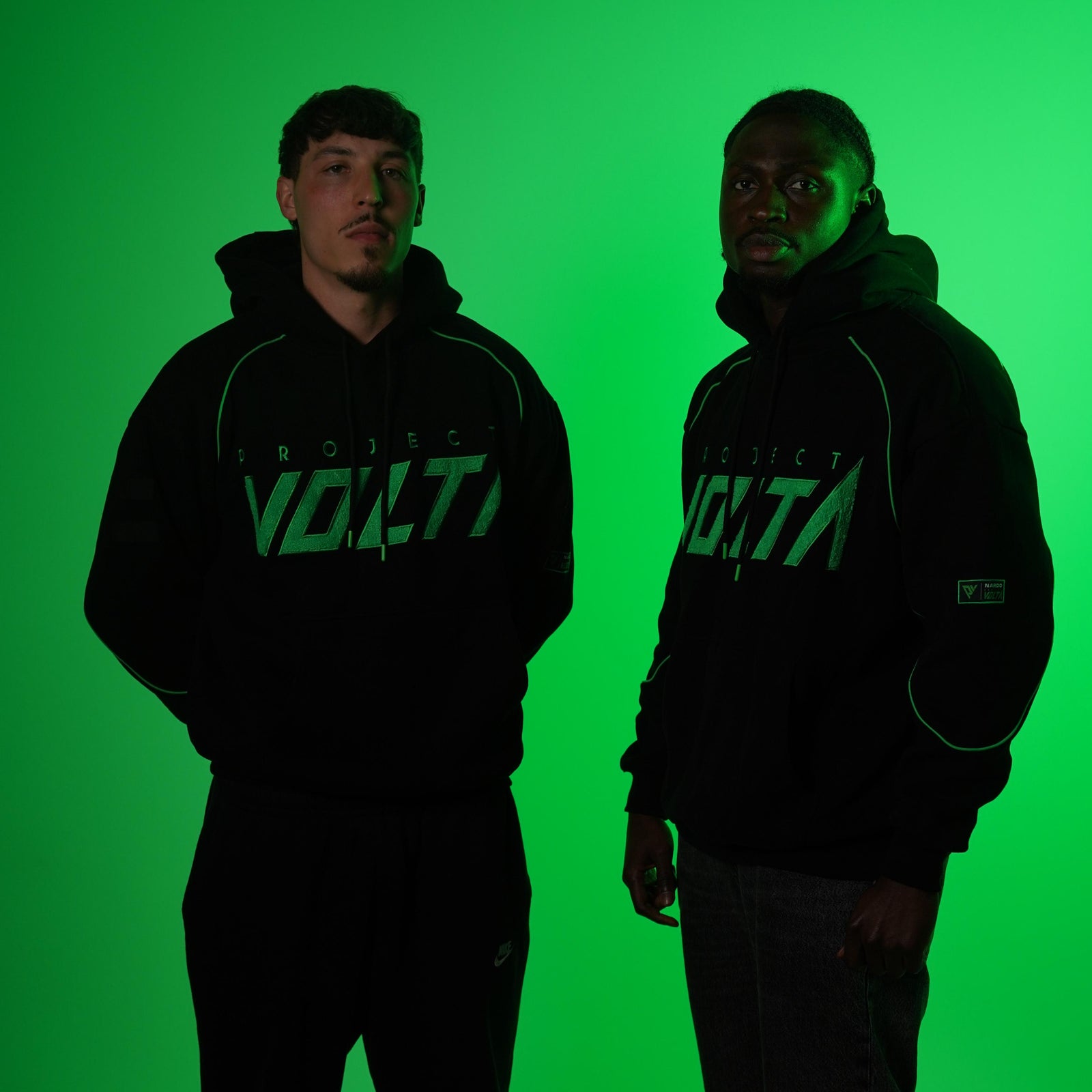 Two people wearing black hoodies with 'Project Volta' logo against a green background