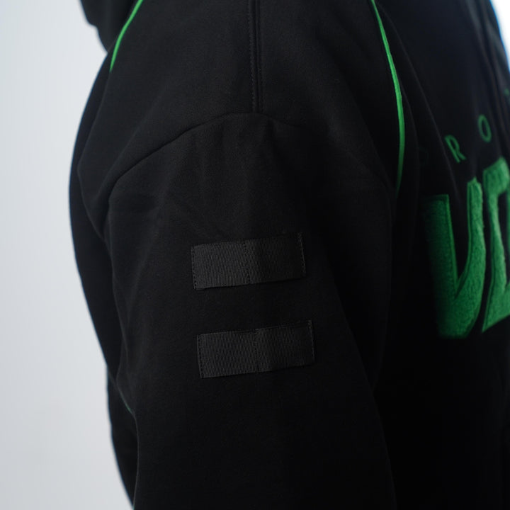 Molle tabs on a black jacket with green accents and branding on a white background
