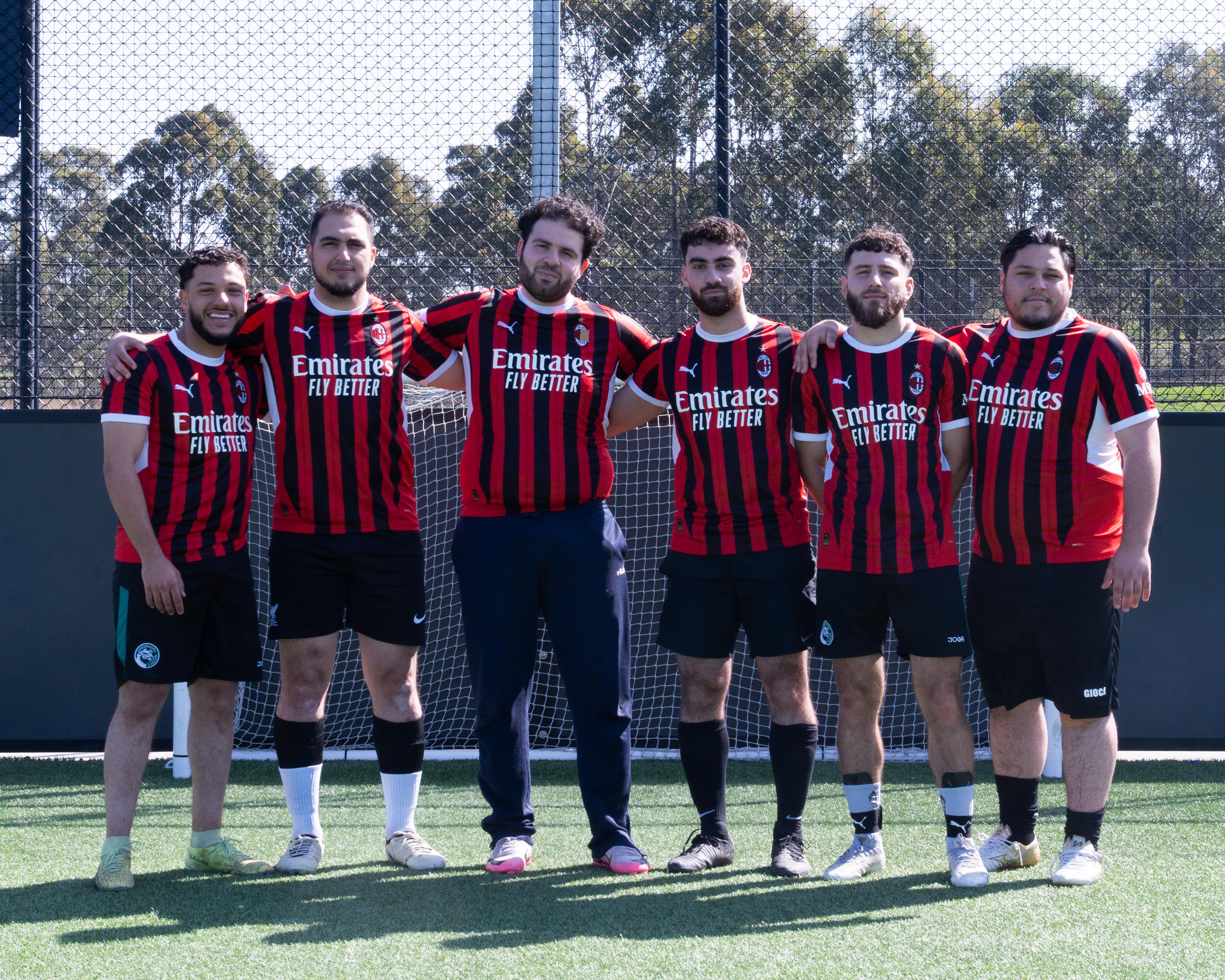 Group of men wearing AC Milan jerseys with on a grassy field.